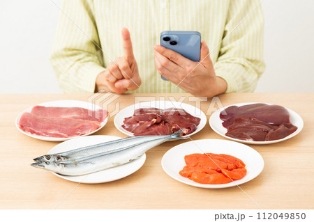 ビタミンB群を多く含む食品とスマホを持って人差し指を立てるミドル女性 112049850