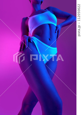 Smooth and healthy skin. View from below of young woman in lingerie in blue neon light against gradient purple background Smooth and healthy skin. View from below of young woman in lingerie in blue neon light against gradient purple background 112050022