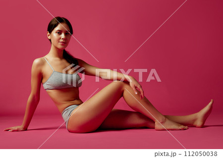 Relaxed and fit woman sitting in gray underwear against vivid pink studio background. Fitness, anti-cellulite program. 112050038