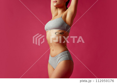 Photo of female model posing raising hands demonstrating her perfect body curves against vivid pink studio background. 112050176