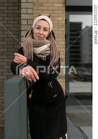 Well-groomed young woman dressed in a winter black coat with a scarf in an urban environment 112051537