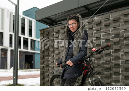 Photo on the street, a young urban informal woman with dreadlocks hairstyle and glasses rides a Photo on the street, a young urban informal woman with dreadlocks hairstyle and glasses rides a 112051549
