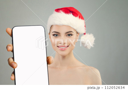 Pretty healthy Christmas woman Santa showing smartphone with empty white screen display Pretty healthy Christmas woman Santa showing smartphone with empty white screen display 112052634