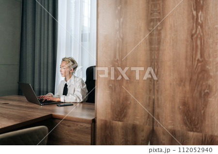 Remote view of focused middle-aged businesswoman sitting at desk typing working on laptop, browse wireless internet. Concentrated elegant senior female employee consult client online using computer. 112052940