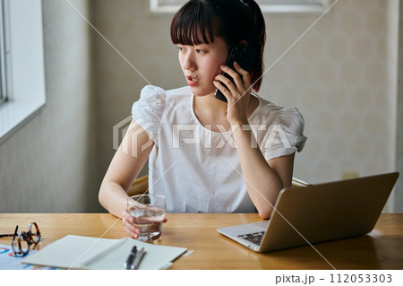 グラスを持ちながら電話をする若い女性 グラスを持ちながら電話をする若い女性 112053303