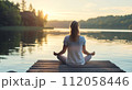 Woman practicing flexible yoga poses and mindful spiritual meditation relaxation near serene lake 112058446