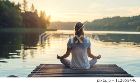 Woman practicing flexible yoga poses and mindful spiritual meditation relaxation near serene lake 112058446