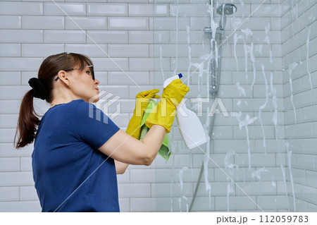 Woman cleaning bathroom, washing glass in shower Woman cleaning bathroom, washing glass in shower 112059783