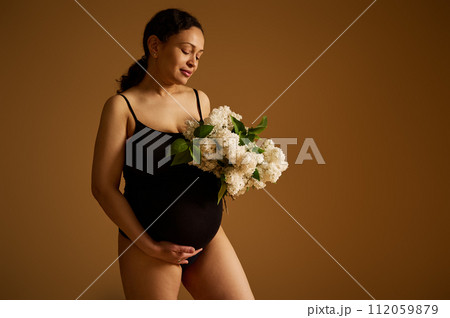 Attractive confident and happy pregnant mother, gravid female in black bodysuit, isolated over beige studio background. Attractive confident and happy pregnant mother, gravid female in black bodysuit, isolated over beige studio background. 112059879