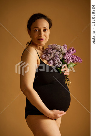 Confident positive pregnant woman in black bodysuit, posing looking at the camera, isolated on beige studio background Confident positive pregnant woman in black bodysuit, posing looking at the camera, isolated on beige studio background 112059884