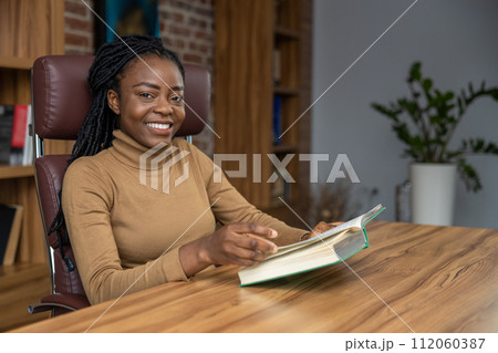 Woman sitting at table reading book student deepening her knowledge for educational purposes Woman sitting at table reading book student deepening her knowledge for educational purposes 112060387