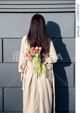 Springtime Mental Health, The Spring Season and Mental Health, Ways to Boost Mental Health for Spring. Back view of Woman Holding Tulips Against Modern Gray Wall 112060542