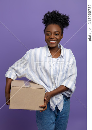 Curly-haired young woman with a box in hand smiling nicely 112060726