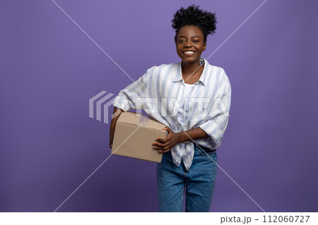 Curly-haired young woman with a box in hand smiling nicely Curly-haired young woman with a box in hand smiling nicely 112060727