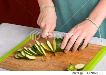 Woman's hands cutting zucchini on wooden cutting board at home, preparing healthy food, close up 112060955