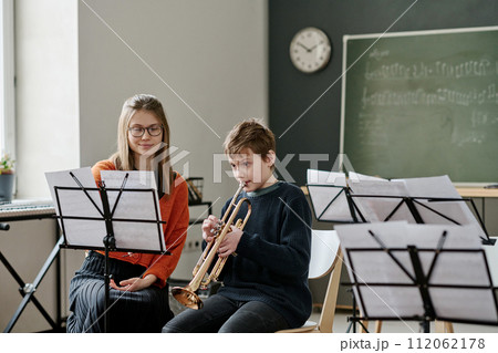 Young Caucasian female music teacher listening to middle school student playing trumpet during class Young Caucasian female music teacher listening to middle school student playing trumpet during class 112062178
