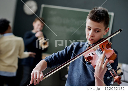 Selective focus dutch angle shot of modern teen boy playing violin during music class at school Selective focus dutch angle shot of modern teen boy playing violin during music class at school 112062182