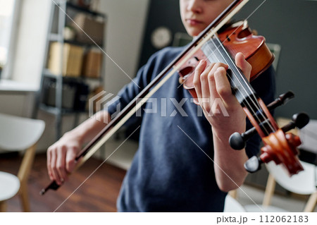 Selective focus dutch angle shot of teen boy practicing violin at music class in classroom Selective focus dutch angle shot of teen boy practicing violin at music class in classroom 112062183