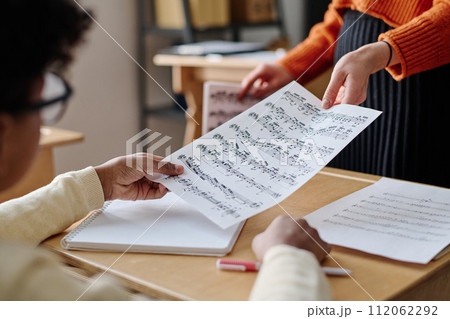 Selective focus medium closeup of unrecognizable teacher giving sheet music to student Selective focus medium closeup of unrecognizable teacher giving sheet music to student 112062292