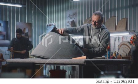 Carpenter makes upholstery of chair using staple gun in furniture workshop 112062931