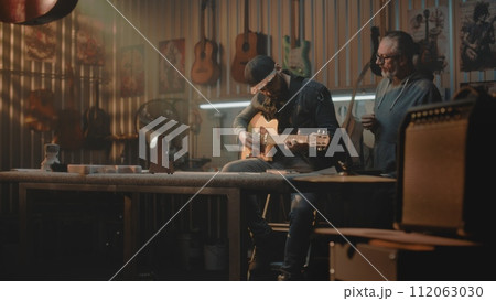 Mature music teacher teaches man to play on guitar in stylish garage studio Mature music teacher teaches man to play on guitar in stylish garage studio 112063030