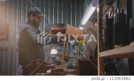 Male craftsman assembles wooden nightstand in furniture workshop 112063062