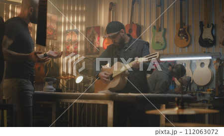 Two woodworking masters make wooden guitar in modern workshop Two woodworking masters make wooden guitar in modern workshop 112063072