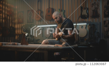 Male musician plays guitar in modern and stylish workshop Male musician plays guitar in modern and stylish workshop 112063087