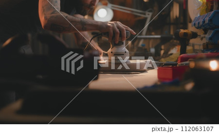 Male carpenter polishes wooden guitar body using polishing machine 112063107