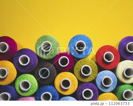 Multicolored threads for sewing and embroidery on yellow background Multicolored threads for sewing and embroidery on yellow background 112063733