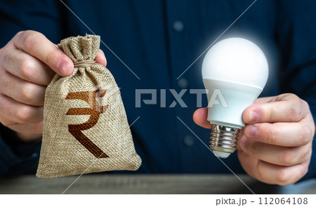 Indian rupee money bag and burning idea light bulb in the hands of a man. Offering financial incentives to enhancing energy efficiency. Reduce carbon footprint. Investment in an idea. Indian rupee money bag and burning idea light bulb in the hands of a man. Offering financial incentives to enhancing energy efficiency. Reduce carbon footprint. Investment in an idea. 112064108