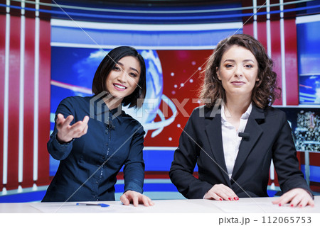 Journalists team discuss daily news, presenting latest events on international television program in newsroom. Two women broadcasters working on entertainment segment with reportage. 112065753