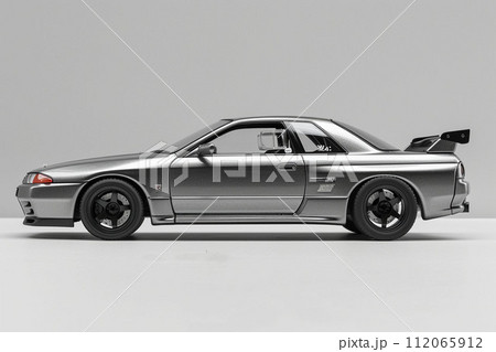 A sleek silver car with shiny alloy wheels parked on a gray surface 112065912