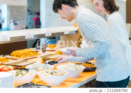 ビュッフェスタイルのレストランで料理を選ぶカップル 112066790