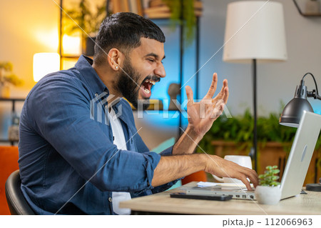 Angry furious Indian man freelancer using laptop working at home office nervous breakdown at work Angry furious Indian man freelancer using laptop working at home office nervous breakdown at work 112066963