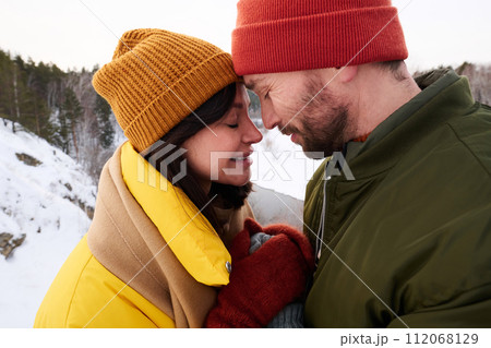 Side view medium closeup of man and woman in love standing with eyes closed and holding hands on winter day 112068129
