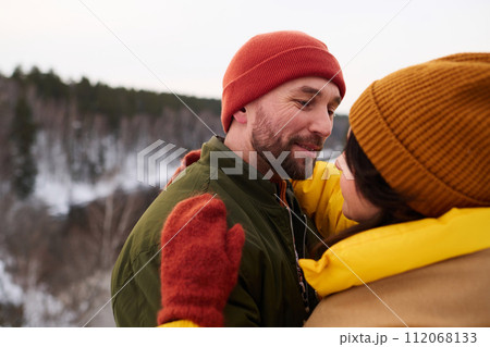 Medium closeup of bearded Caucasian man hugging his wife while standing outdoors on winter day Medium closeup of bearded Caucasian man hugging his wife while standing outdoors on winter day 112068133