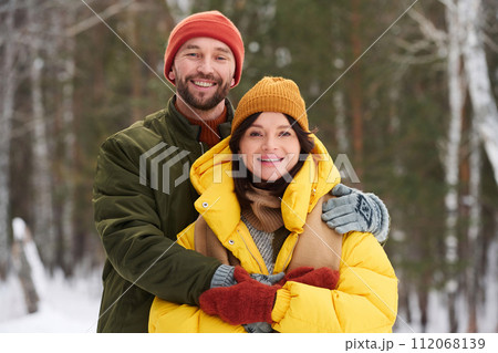Medium portrait of happy Caucasian man and woman in love standing outdoors smiling at camera on winter day Medium portrait of happy Caucasian man and woman in love standing outdoors smiling at camera on winter day 112068139