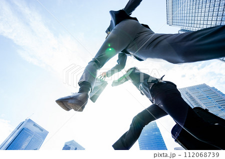 大都会で青空に向かって2人のチームで飛翔しジャンプするダイナミックで勢いのあるビジネスマンの男性 112068739