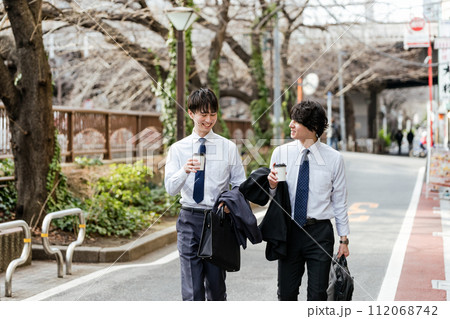 会話しながらテイクアウトカップを持って歩く2人の若いビジネスマンの男性 112068742