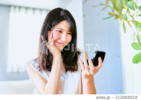 自宅にて出勤前に朝のスキンケアの調子を鏡で見て嬉しい表情をするナチュラルや雰囲気の30代の笑顔の女性 112068918