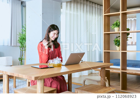自宅リビングのテーブルにノートパソコンを広げオンライン講座を受講する笑顔の30代の女性 112068923