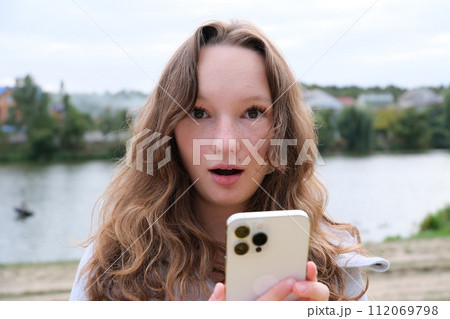 Young blonde woman using mobile phone with surprise facial expression. High quality photo Young blonde woman using mobile phone with surprise facial expression. High quality photo 112069798