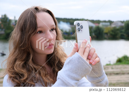 Red-haired young girl taking selfie with her smartphone against snowy background. Selective focus. High quality photo 112069812