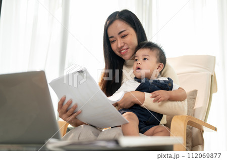 A busy Asian working woman mom is focusing on her work and taking care of her cute little son. 112069877
