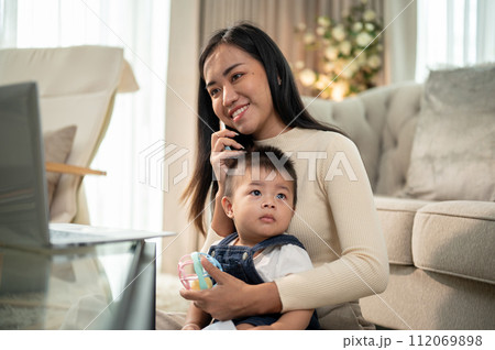 A positive Asian businesswoman mom is talking on the phone while taking care of her little son. 112069898