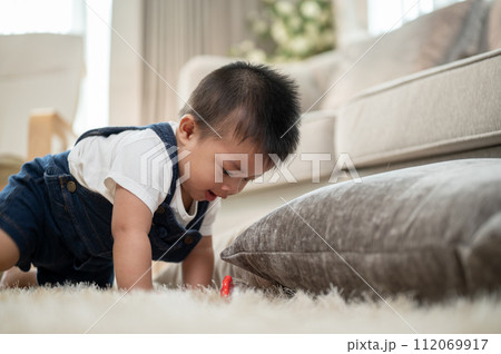 A cute, cheerful Asian baby boy is playing with toys and crawling on the floor in the living room. A cute, cheerful Asian baby boy is playing with toys and crawling on the floor in the living room. 112069917
