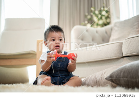 A cute, cheerful Asian baby boy is playing with toys on a carpet in the living room. 112069918