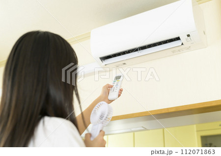 エアコンを操作する暑がっている女性(リモコンにピント) エアコンを操作する暑がっている女性(リモコンにピント) 112071863