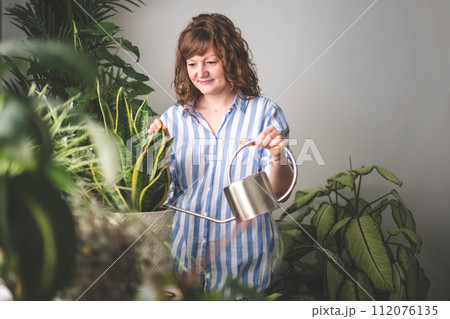 A young woman enjoys caring for flowers. Watering indoor plants and admiring them. A young woman enjoys caring for flowers. Watering indoor plants and admiring them. 112076135
